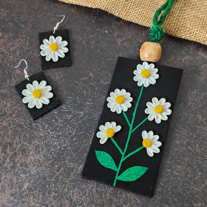 Avani fabric necklace set — black cotton pendant with raised hand-shaped clay daisies and hand-painted leaves and stems, with matching earrings