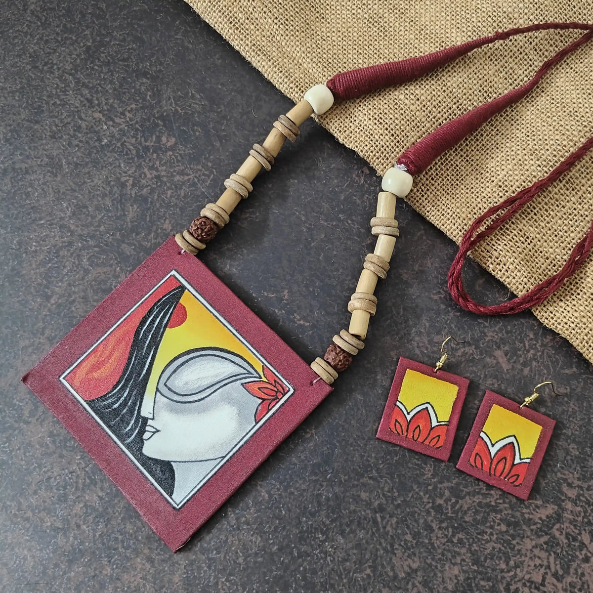 Kalavati maroon fabric necklace set — maroon cotton pendant hand-painted with a woman's face wearing kumkum and flowers, with matching dangler earrings