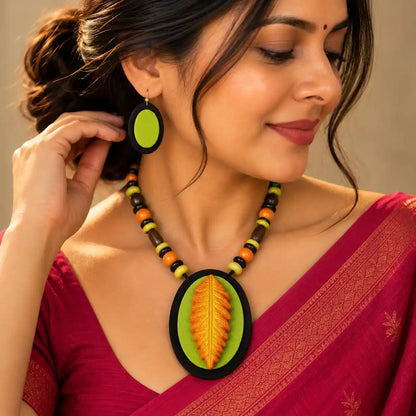 Nirmita black fabric necklace set — oval black pendant with a green fabric applique and a hand-shaped clay leaf in yellow and orange, with oval dangler earrings