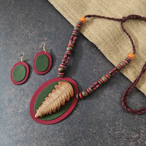 Nirmita maroon fabric necklace set — oval maroon pendant with a green fabric applique and a hand-shaped clay leaf in brown and beige, with oval dangler earrings