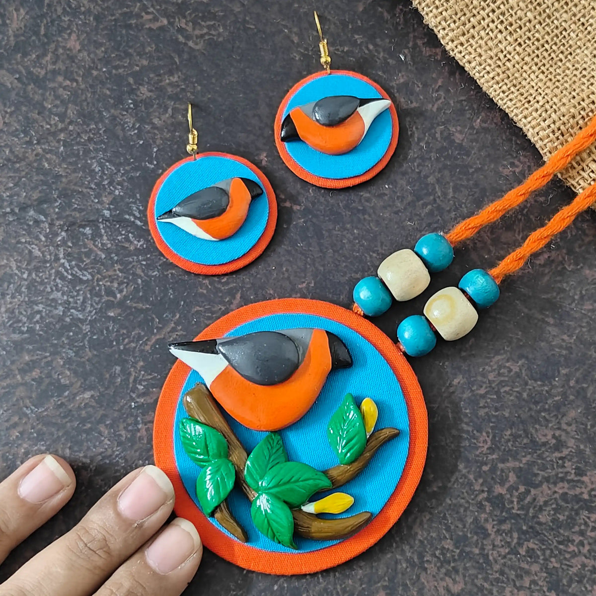 Parthivi fabric necklace set — round pendant with a blue circle appliqued on orange fabric and a nature scene modelled in clay, with clay bird earrings