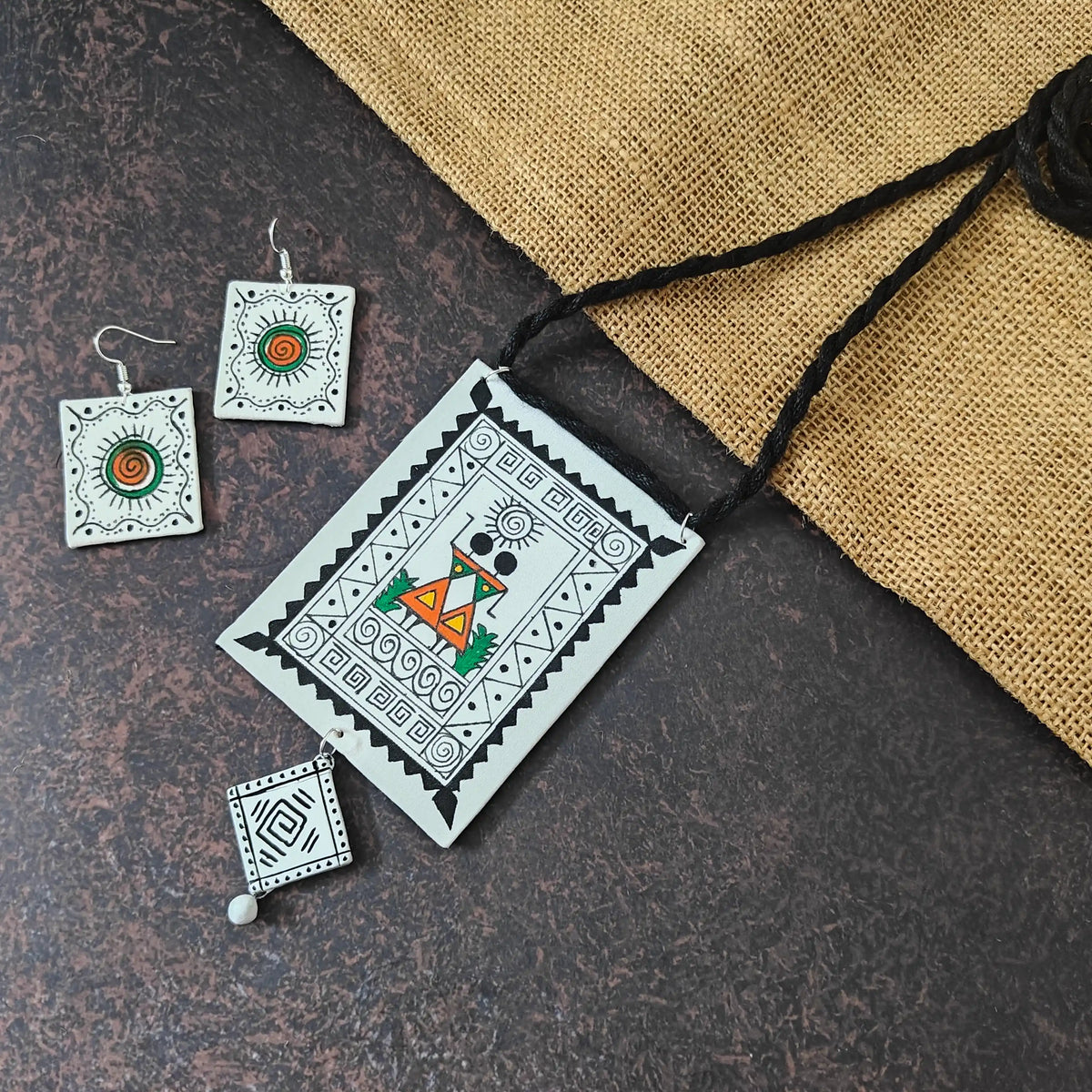 Shilpika fabric necklace set — rectangular cotton pendant hand-painted with two Warli women, with a painted square clay dangle and sun-motif earrings