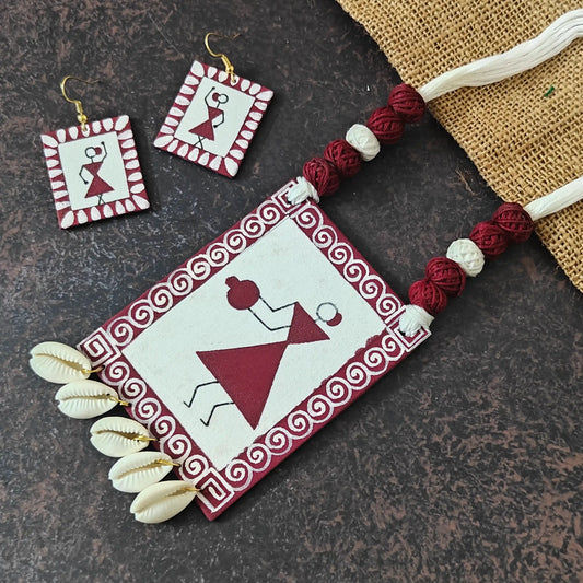 Udaya fabric necklace set — white cotton pendant hand-painted with a maroon Warli woman carrying a pot, with cowrie shell dangles and matching rectangular earrings